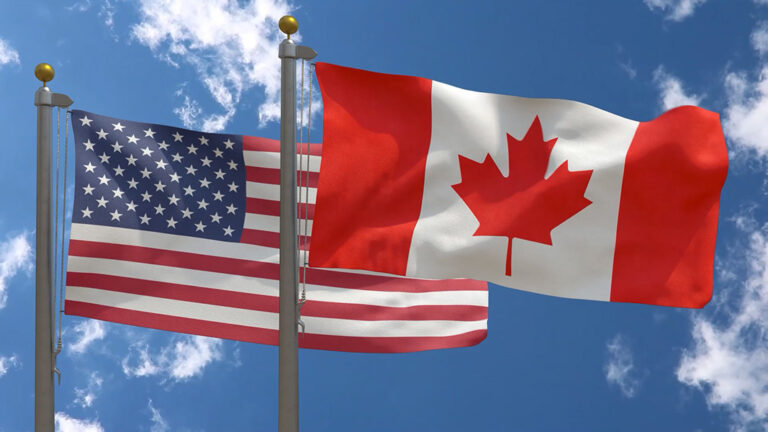 American & Canadian Flags waving in front of a clear blue sky