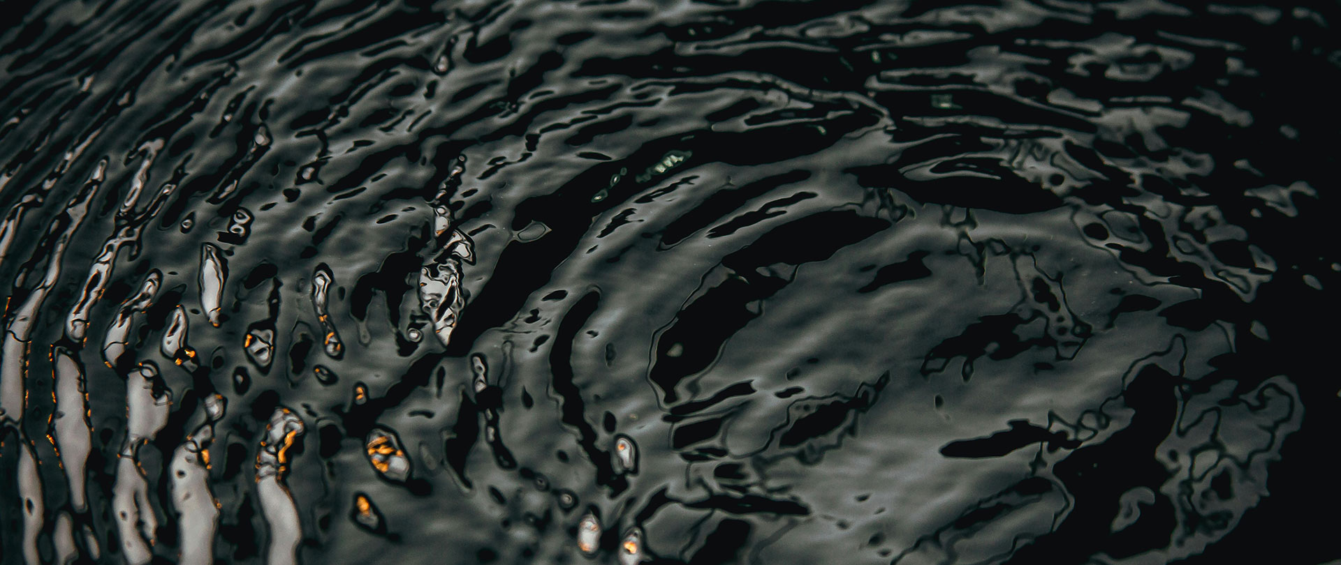 Close-up of dark water with ripples, reflecting subtle highlights from light sources.