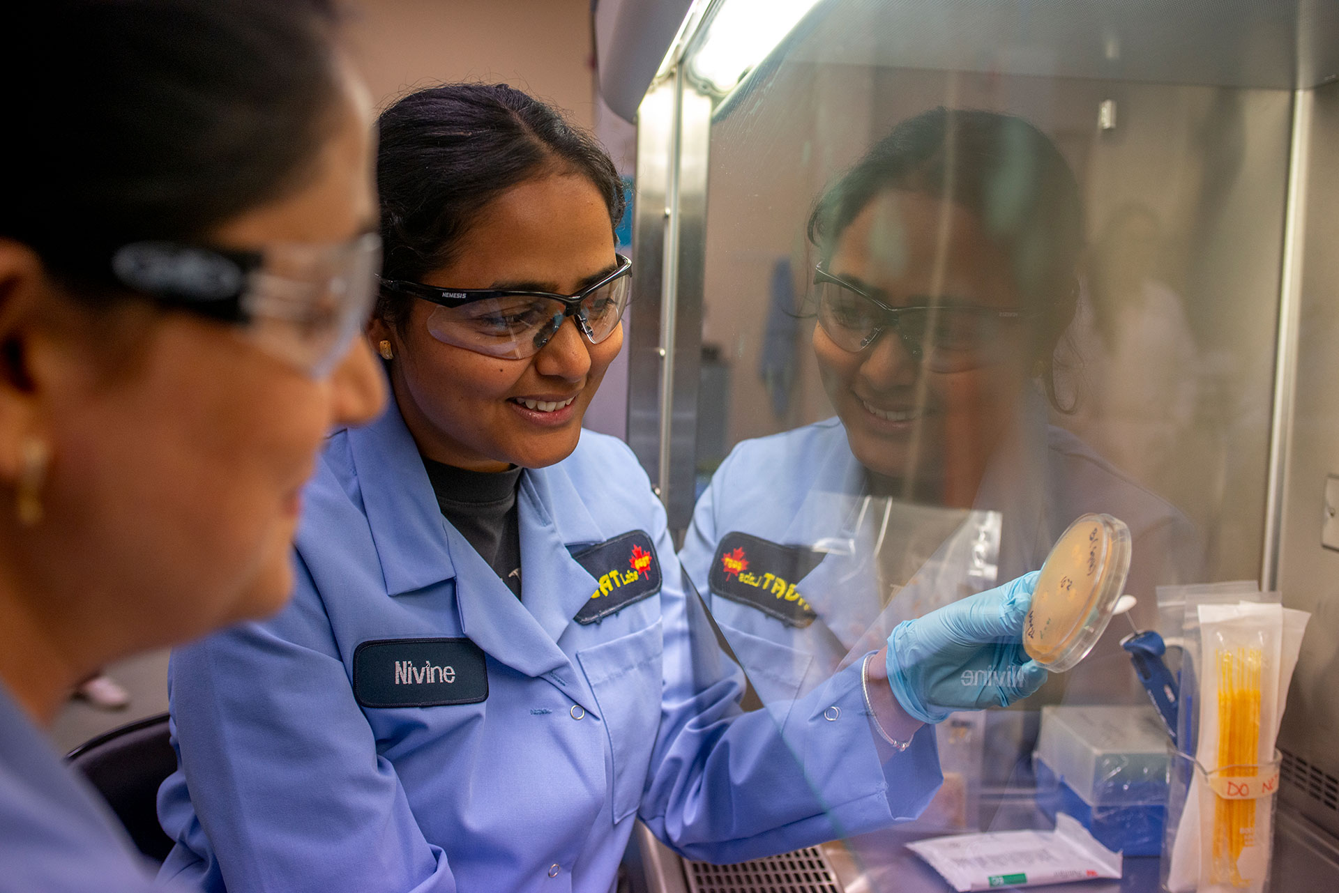 A group of AGAT Laboratories employees wearing lab coats, safety goggles, and gloves, smiling and posing together in a laboratory setting.