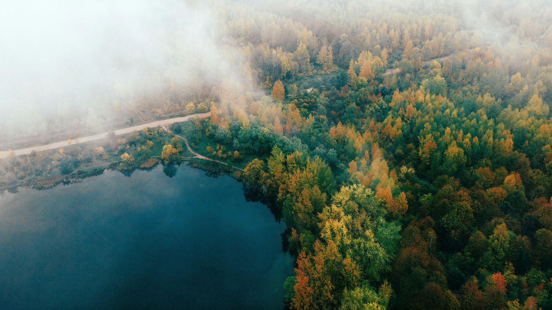Un lac calme entouré d'une forêt d'automne avec du brouillard roulant sur les arbres.